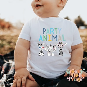 May include: White baby onesie with the text "PARTY ANIMAL" in blue, green, and yellow. Three cartoon animals, a zebra, elephant, and giraffe, are wearing party hats and accessories.