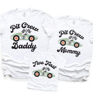 Pu&ograve; includere: Tre magliette bianche con un design di auto da corsa verde e testo. Le magliette dicono "Pit Crew Daddy", "Pit Crew Mommy" e "Two Fast".