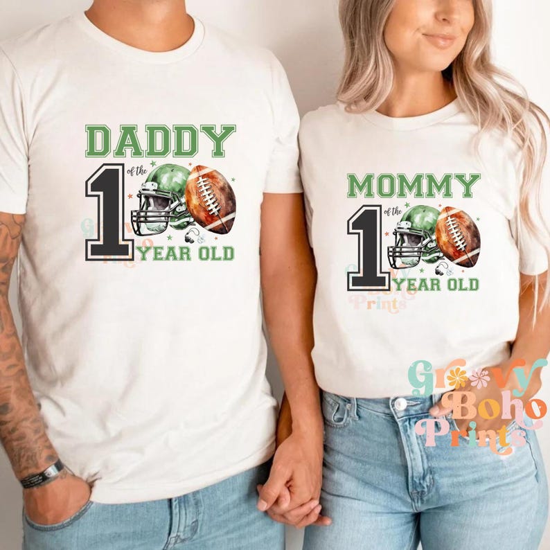May include: White t-shirts with green and black text that reads "Daddy of the 1 Year Old" and "Mommy of the 1 Year Old".  Each shirt features a football helmet and football with watercolor-style green and brown accents.