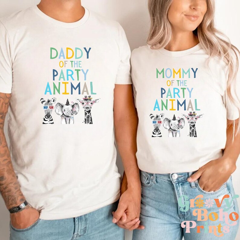 Puede incluir: Dos camisetas blancas con un dise&ntilde;o gr&aacute;fico de una cebra, un elefante y una jirafa con sombreros de fiesta. El texto en las camisetas dice "Daddy of the Party Animal" y "Mommy of the Party Animal".