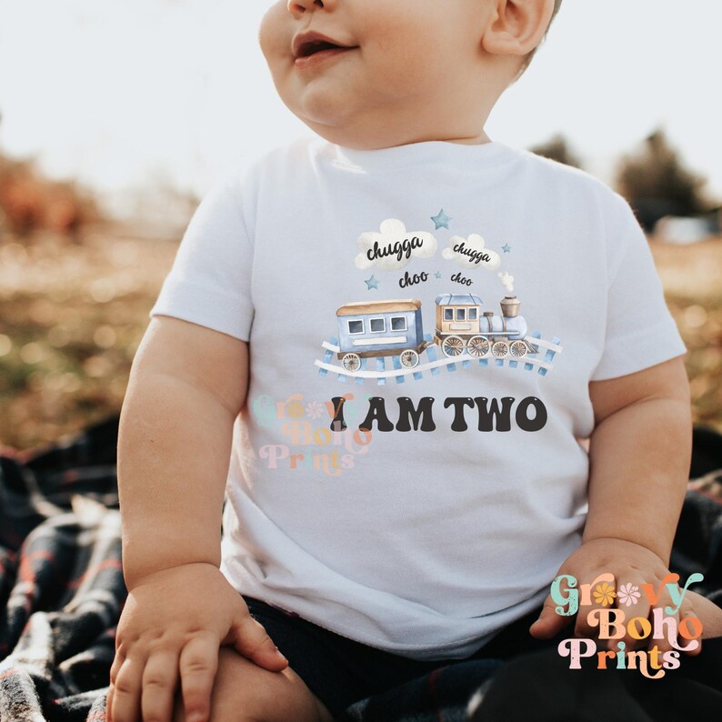 May include: A white toddler shirt with a blue train design and the text "I am two" in black. The train has clouds above it with the text "chugga choo" on each cloud.