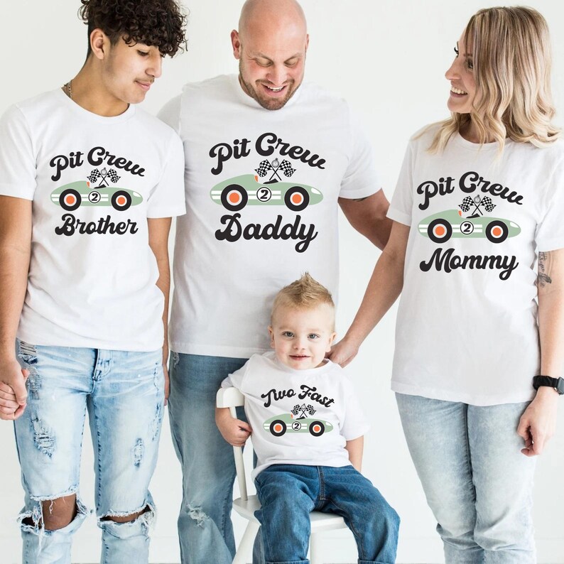 Pu&ograve; includere: Un set di quattro t-shirt bianche con una grafica di auto da corsa verde e testo che recita "Pit Crew Brother", "Pit Crew Daddy", "Pit Crew Mommy" e "Two Fast".