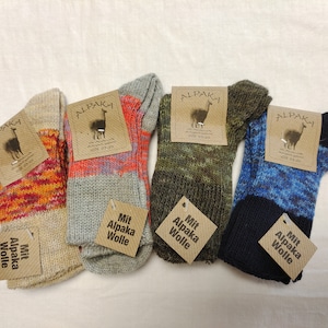 May include: Four pairs of socks with different colored patterns. Each sock is made with alpaca wool and has a tag that says "Mit Alpaka Wolle".