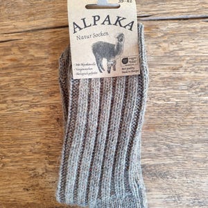 May include: A pair of gray ribbed knit socks with a tag that reads "ALPAKA Natur Socken" and features an alpaca illustration. The socks are size 39-42 and made in Europe.
