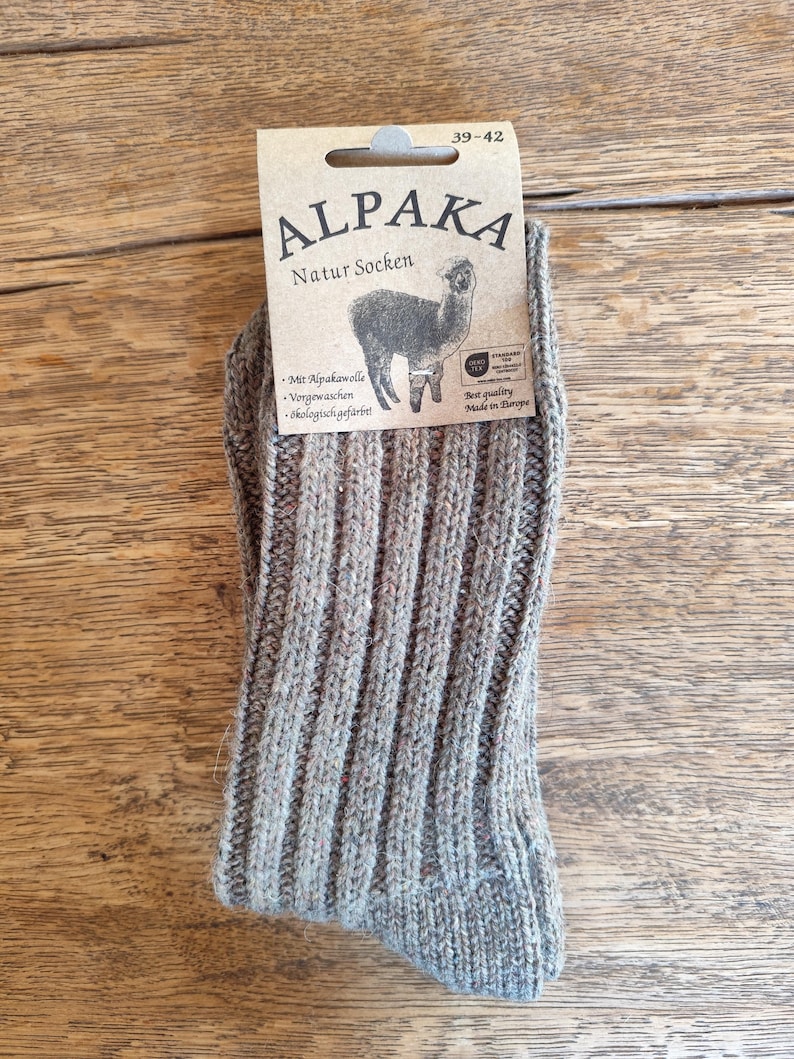 May include: A pair of gray ribbed knit socks with a tag that reads "ALPAKA Natur Socken" and features an alpaca illustration. The socks are size 39-42 and made in Europe.