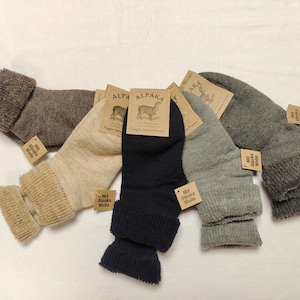 May include: Five pairs of alpaca wool socks in various colors, including brown, beige, black, and gray. Each sock has a fold-over cuff and a tag that reads "Alpaca Wool".