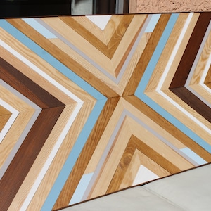 May include: A geometric wall art piece made of wood with a chevron pattern. The wood is painted in shades of brown, white, and light blue.
