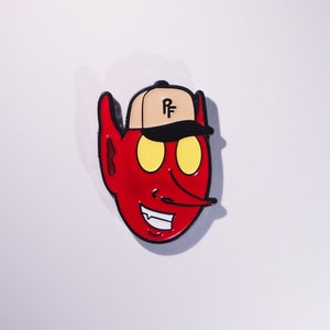 Puede incluir: Cabeza de diablo de dibujos animados roja con contorno negro y ojos amarillos que lleva una gorra de béisbol de color beige con las letras "PF" en negro.
