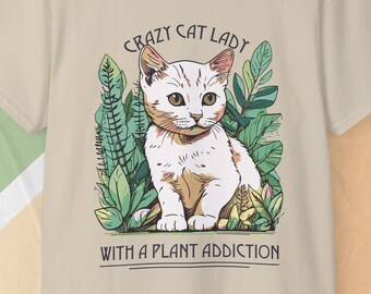 May include: A beige t-shirt with a white cat illustration and green plants. The text "Crazy Cat Lady with a Plant Addiction" is printed below the cat.