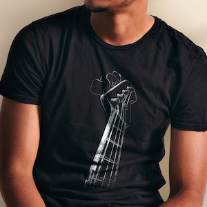 Peut inclure: T-shirt noir avec un motif blanc détaillé du manche et de la tête d'une basse. Le design met en valeur les cordes et les chevilles d'accord. Le t-shirt à manches courtes est fabriqué dans une matière douce.