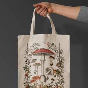 May include: A white canvas tote bag with a colorful illustration of mushrooms and foliage. The mushrooms are red, white, and brown with green stems. The foliage is green and brown.