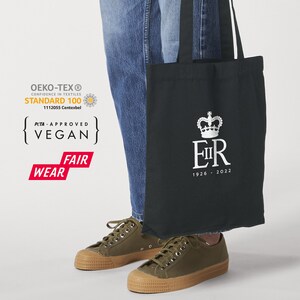 May include: Black tote bag featuring a white crown and the letters "E II R" with the dates "1926 - 2022". The bag is made of canvas and has a vegan certification label.