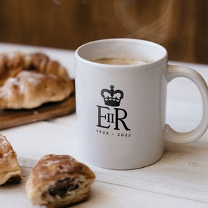 May include: White ceramic mug with a black crown and the letters "EIIR" and the text "1926 - 2022". The mug is filled with coffee and steam is rising from the mug.