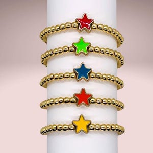 May include: Five gold bracelets with star charms. The stars are red, green, blue, orange, and yellow.