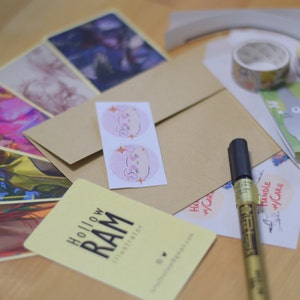 Puede incluir: Un surtido de impresiones art&iacute;sticas, pegatinas y art&iacute;culos de papeler&iacute;a. Incluye una tarjeta de visita con el texto "Hollow RAM Illustrator", cinta adhesiva con estampado floral y un rotulador dorado. Los art&iacute;culos est&aacute;n dispuestos sobre una superficie clara.