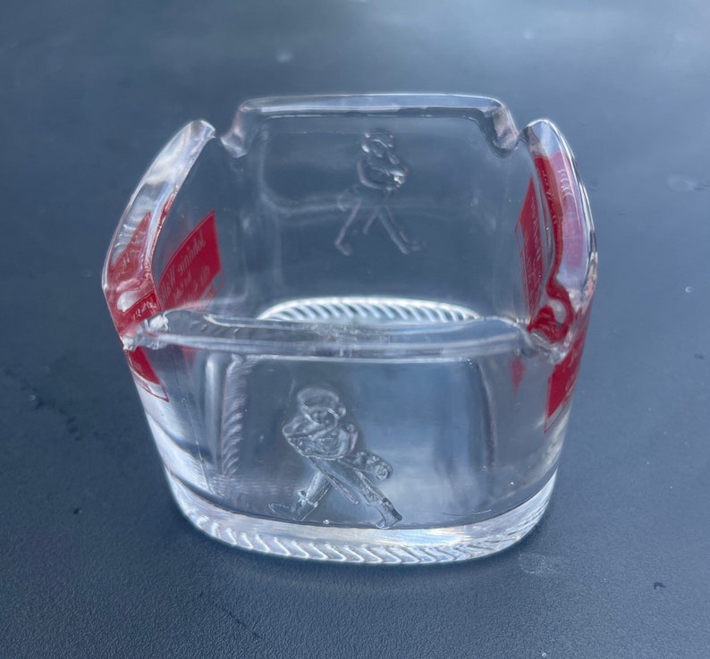 May include: A clear glass ashtray with a red and white label that says "Johnnie Walker Red Label" and a raised image of a man walking with a cane.