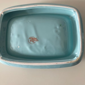 May include: A rectangular, light blue ceramic dish with rounded corners and a white rim. The interior is a solid, pale blue. The bottom of the dish has a red and white logo that reads "Wade Regicor, England".