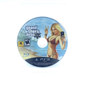 May include: A blue-ray disc for the video game Grand Theft Auto V. The disc features a woman in a bikini taking a selfie on a beach. The game is rated M for Mature by the ESRB.