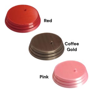 K&ouml;nnte beinhalten: Drei kreisf&ouml;rmige Pr&auml;sentationsst&auml;nder mit einem kleinen zentralen Stift, jeder mit einem abgestuften Sockeldesign. Die St&auml;nder sind in drei verschiedenen Farben erh&auml;ltlich: Rot, Kaffeegold und Pink, wobei die Farbnamen daneben gedruckt sind.