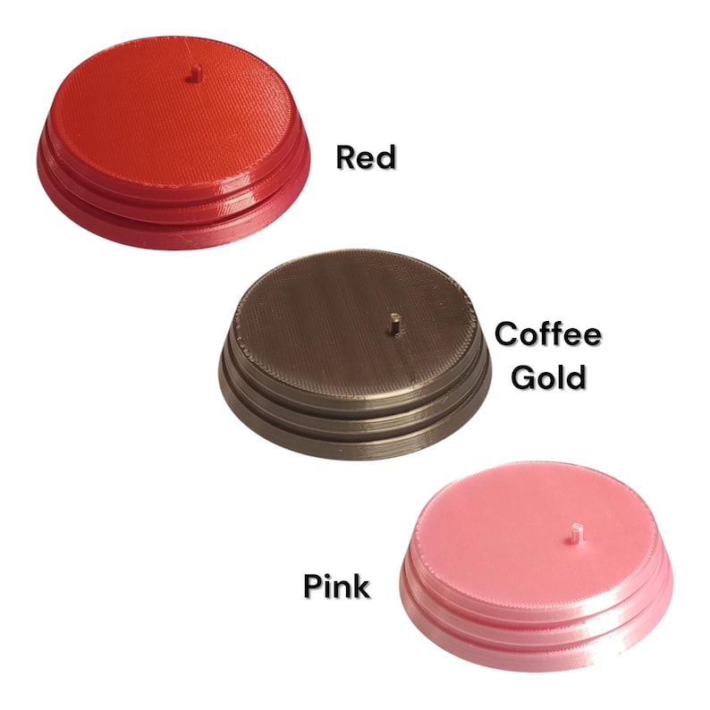 K&ouml;nnte beinhalten: Drei kreisf&ouml;rmige Pr&auml;sentationsst&auml;nder mit einem kleinen zentralen Stift, jeder mit einem abgestuften Sockeldesign. Die St&auml;nder sind in drei verschiedenen Farben erh&auml;ltlich: Rot, Kaffeegold und Pink, wobei die Farbnamen daneben gedruckt sind.