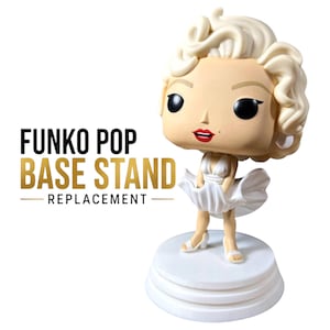 K&ouml;nnte beinhalten: Eine Vinylfigur einer blonden Frau mit einem Sch&ouml;nheitsfleck, die ein wei&szlig;es Kleid tr&auml;gt und auf einem runden wei&szlig;en Sockel steht. Der Text FUNKO POP BASE STAND REPLACEMENT ist links neben der Figur in Schwarz und Gold gedruckt.
