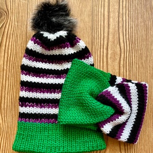 May include: A green and purple striped knit hat with a black pom pom and a matching green and purple striped knit headband.