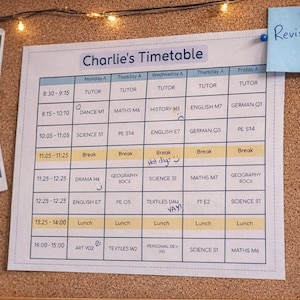 Könnte beinhalten: Eine Pinnwand mit einem Stundenplan mit der Aufschrift "Charlie's Timetable". Ein blauer Haftzettel mit der Aufschrift "Revision!". Ein blaues Headset und ein Stapel Bücher liegen auf einem Holztisch. Ein Gamecontroller und Stifte sind ebenfalls zu sehen.