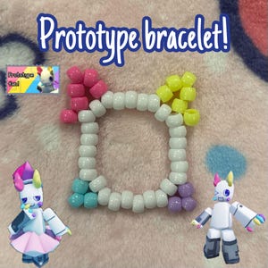 May include: A colorful beaded bracelet with the text "Prototype bracelet!" in a playful font. The bracelet features a square design with white, pink, yellow, light blue, and purple beads. Two cartoon figures are also in the image.