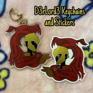 May include: Keychains and stickers featuring a stylized illustration of a figure with a gold helmet and red cape. The keychain has a gold clasp. The text "D3rLord3 Keychains and Stickers" is displayed in the image.