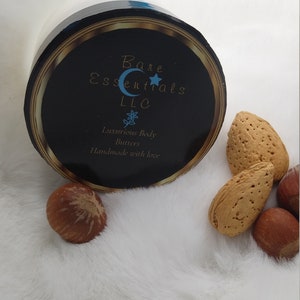 May include: A white jar with a black lid and gold trim. The lid has a label that says "Bare Essentials LLC" with a blue crescent moon and star. The label also says "Luxurious Body Butters" and "Handmade with love".