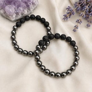 Puede incluir: Dos pulseras de cuentas con secciones alternas de cuentas de piedra de lava negra, redondas y porosas, y cuentas de hematita gris metálico, lisas y reflectantes. Las pulseras son circulares y están hechas con un cordón flexible.