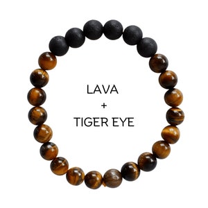 Può includere: Un braccialetto fatto di perline marroni di occhio di tigre e perline nere di lava. Il braccialetto ha il testo "LAVA + TIGER EYE" al centro.
