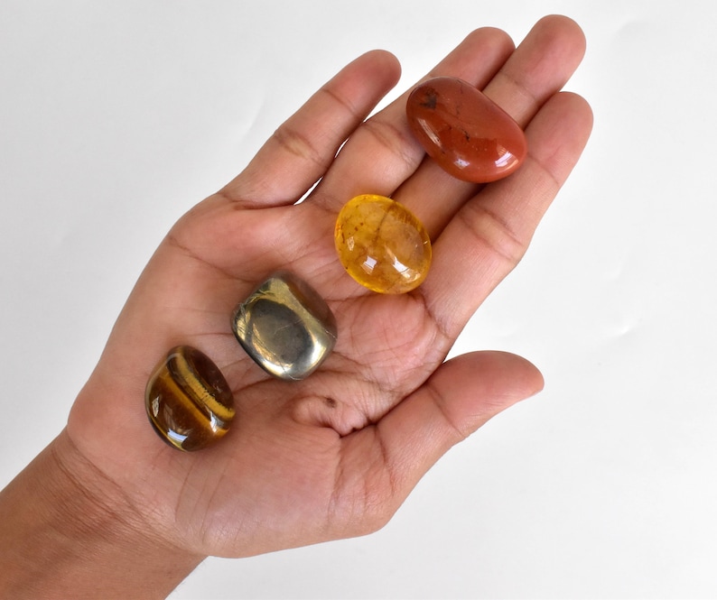 Pode incluir: Uma cole&ccedil;&atilde;o de quatro pedras polidas: uma jaspe vermelha, um olho de tigre dourado, uma citrina clara e uma pirita met&aacute;lica.