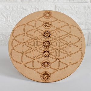 May include: A wooden round mandala with a flower of life design and seven chakras symbols engraved in the center.