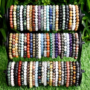 May include: A display of colorful gemstone bracelets on a black stand. The bracelets are made of various types of stones, including amethyst, agate, and jasper.