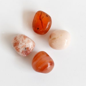 May include: Four tumbled stones, two are orange-red and two are light pink. The stones are smooth and polished.