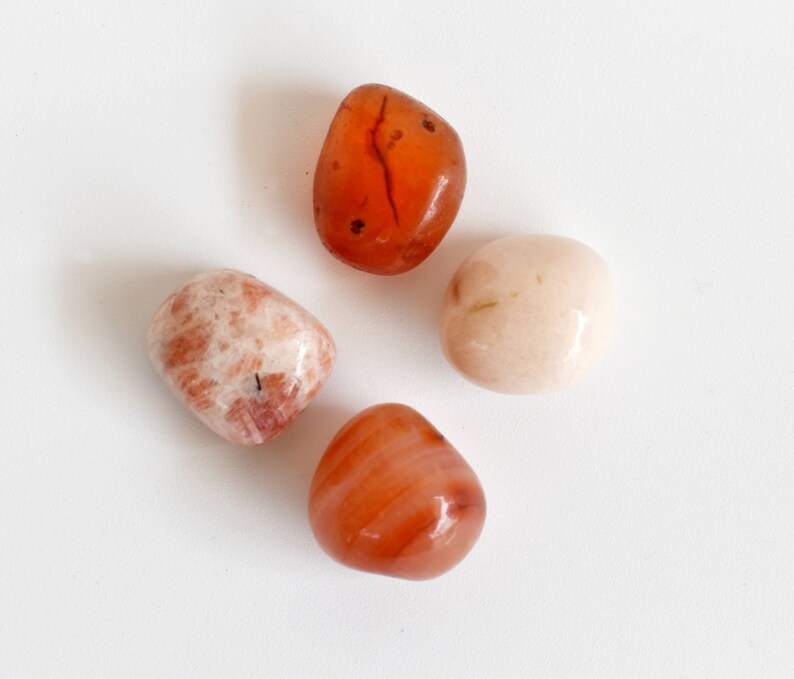 May include: Four tumbled stones, two are orange-red and two are light pink. The stones are smooth and polished.