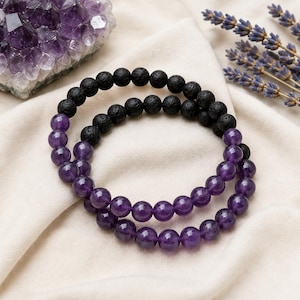May include: Two beaded bracelets featuring a combination of round, porous black lava stone beads and smooth, translucent purple amethyst beads. The bracelets are arranged in a circular pattern, showcasing the contrast between the dark texture.