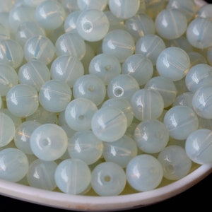 May include: A bowl filled with white opaque round beads. The beads have a slight iridescent sheen.