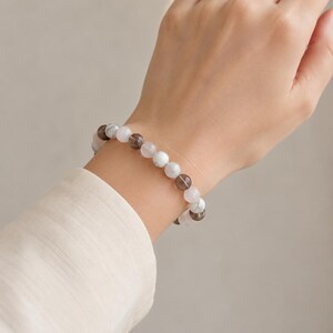 Puede incluir: Una pulsera de cuentas con esferas alternas en color marr&oacute;n ahumado transl&uacute;cido y blanco opaco con vetas grises. Las cuentas est&aacute;n ensartadas en un cord&oacute;n el&aacute;stico, formando una banda circular con un acabado suave y pulido en la mu&ntilde;eca.