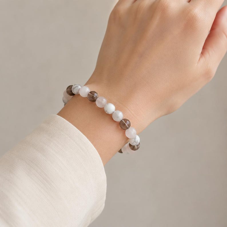 Puede incluir: Una pulsera de cuentas con esferas alternas en color marr&oacute;n ahumado transl&uacute;cido y blanco opaco con vetas grises. Las cuentas est&aacute;n ensartadas en un cord&oacute;n el&aacute;stico, formando una banda circular con un acabado suave y pulido en la mu&ntilde;eca.