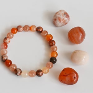 May include: A bracelet made of orange, brown and white beads. The bracelet is surrounded by four loose stones: one white, two orange and one brown.