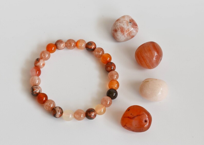 May include: A bracelet made of orange, brown and white beads. The bracelet is surrounded by four loose stones: one white, two orange and one brown.