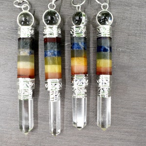 Może przedstawiać: Cztery srebrne i kryształowe wahadła czakr z siedmioma warstwami kamieni szlachetnych. Każde wahadło ma ostry kryształowy czubek, srebrną czapkę i przezroczystą kryształową kulę na górze.