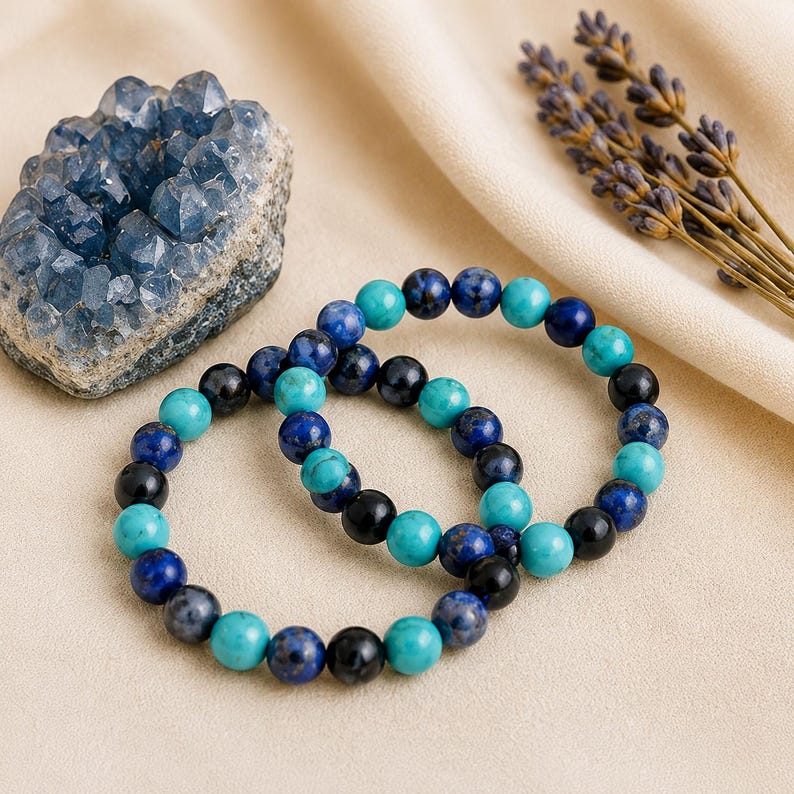 May include: Two stretch bracelets composed of round beads in shades of turquoise, deep blue, and black. The beads are arranged in a repeating pattern, creating a colorful contrast. The bracelets are displayed alongside a blue crystal cluster.
