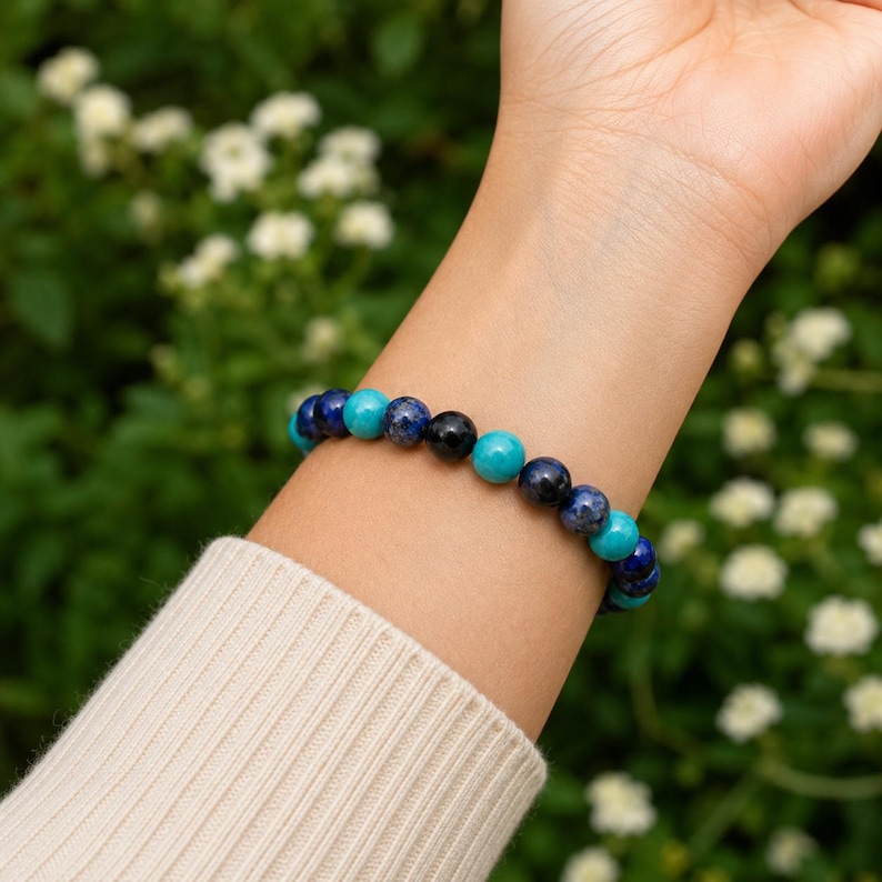 May include: A beaded bracelet featuring alternating round polished stones in shades of deep royal blue, dark navy, and bright turquoise. The beads are strung on an elastic cord, creating a circular band that fits snugly around the wrist area.