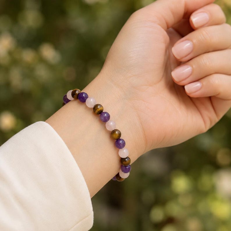 May include: A beaded bracelet featuring a repeating pattern of round, polished gemstones in shades of deep purple amethyst, golden-brown tiger's eye, and pale pink rose quartz, strung together on a flexible cord worn around the wrist.