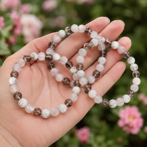 Puede incluir: Dos pulseras el&aacute;sticas de cuentas con cuentas redondas alternas de cuarzo ahumado transl&uacute;cido y piedra blanca opaca veteada. Las cuentas son pulidas y lisas, dispuestas en un patr&oacute;n repetitivo para crear un dise&ntilde;o circular para la mu&ntilde;eca.
