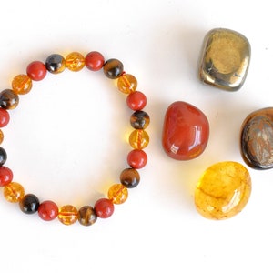 Pode incluir: Um bracelete feito de contas vermelhas, amarelas e marrons. O bracelete &eacute; rodeado por quatro pedras soltas: uma pedra vermelha, uma pedra amarela, uma pedra marrom e uma pedra dourada.