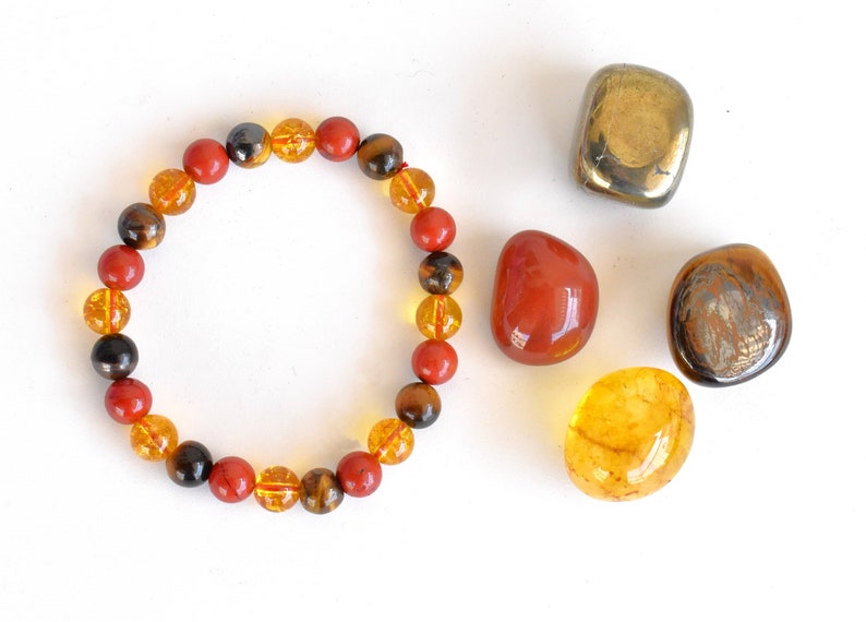 Pode incluir: Um bracelete feito de contas vermelhas, amarelas e marrons. O bracelete &eacute; rodeado por quatro pedras soltas: uma pedra vermelha, uma pedra amarela, uma pedra marrom e uma pedra dourada.